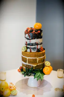 two tier naked wedding cake with sliced kiwis, fresh berries and clementines