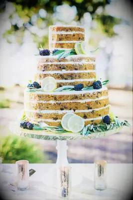 three tier naked wedding cake decorated with bay leaves, sliced lemons and blackberries