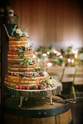 naked wedding cake on top of wooden wine barrel with tiers aligned to the left and decorated with fresh fruit