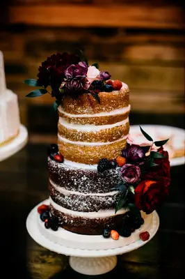 two tier winter naked wedding cake with powdered sugar, fresh berries and burgundy flowers