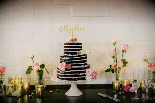 three tier chocolate naked wedding cake with pink and ivory roses and gold mr & mrs. cake topper