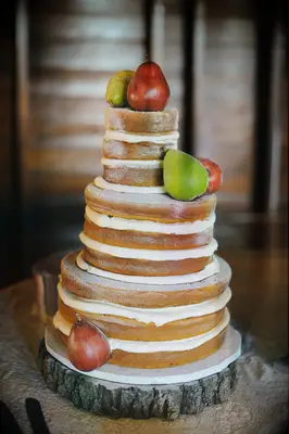 three tier naked wedding cake on wooden cake stand decorated with red and green pears