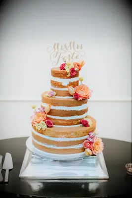 three tier vanilla sponge naked wedding cake on silver stand decorated with pink and orange flowers and gold mr & mrs. cake topper