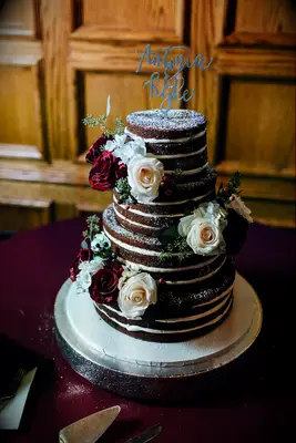 chocolate naked wedding cake decorated with white and red roses and eucalyptus