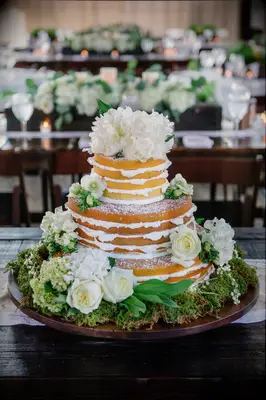 vanilla naked wedding cake decorated with white flowers, powdered sugar and moss base at the bottom tier