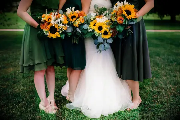 Bridesmaids in green dresses with bride holding burnt orange and sunflower bouquets