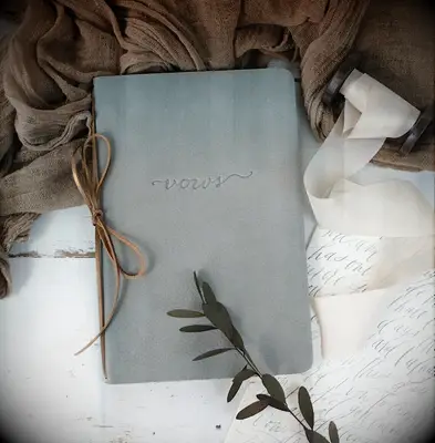 gray leather vow book embossed with vows in cursive script on the front and tied with brown leather binding