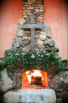 simple wedding fireplace decor idea with wooden cross and greenery on stone hearth