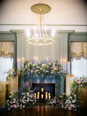 romantic wedding fireplace decor idea with pastel pink, purple and blue flowers, greenery and tall taper candles with glass covers