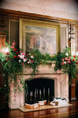 wedding fireplace decor with greenery vines and pink and red roses on top of stone mantel