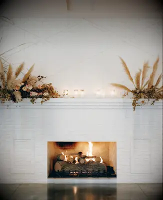 boho wedding fireplace decoration idea with pampas grass, dried flowers and votive candles against white brick mantel