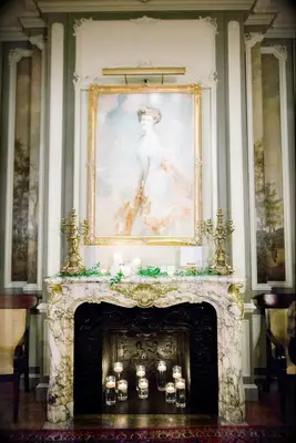 elegant wedding fireplace with marble and gold carved mantel, antique oil painting and simple greenery with votive candles