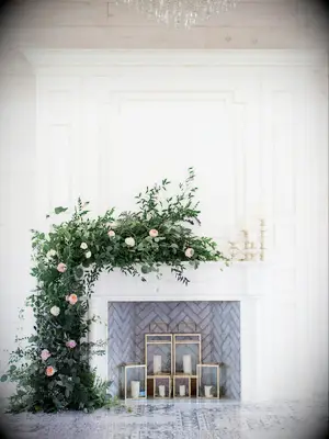 white wedding fireplace decorated with greenery, blush roses and white candles in gold square lanterns