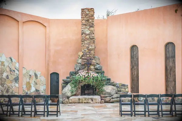 outdoor wedding fireplace made from stones decorated with wooden cross, pink garden roses and greenery vines