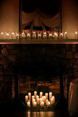 stone wedding fireplace decorated with white pillar candles and floating candles in glass vases