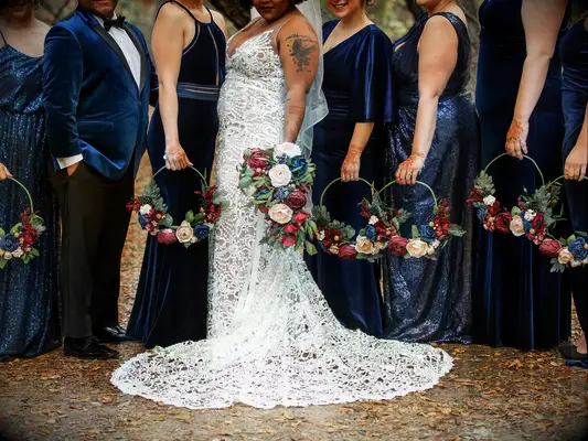 bridesmaids wearing mix and match navy blue gowns hold hoop bouquets with burgundy, blush and blue faux flowers