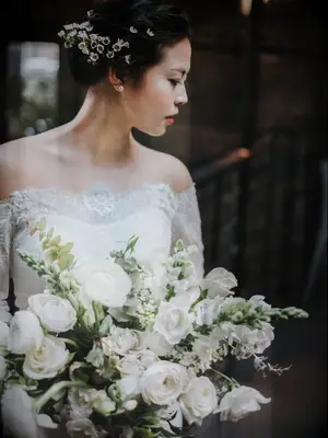 bride holding white winter wedding bouquet and small white flowers in her updo hairstyle