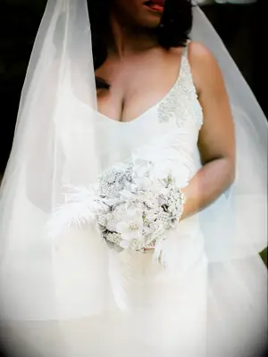 bride holding alternative unique winter wedding bouquet made of silver rhinestone brooches with white feathers 