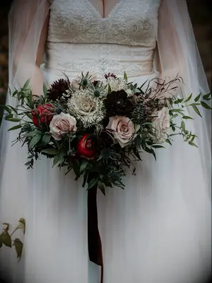 winter wedding bouquet with greenery, mauve roses, burgundy dahlias, blue thistle and pomegranates