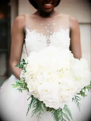 bride holds oversized round wedding bouquet with white roses and winter evergreens around the bottom