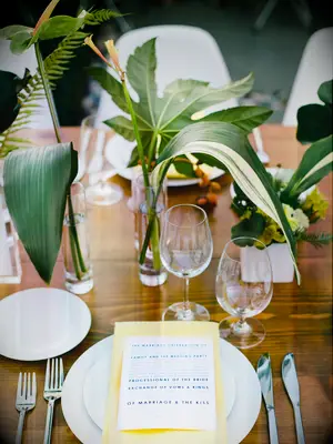 tropical wedding centerpiece with banana leaves and greenery in bud vases