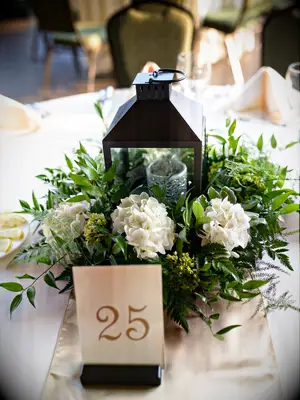 wedding centerpiece with bronze hurricane lantern, white hydrangeas and fresh smilax vines