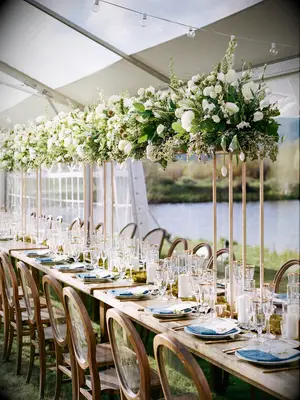 long wooden wedding reception table decorated with tall greenery and white flower centerpieces