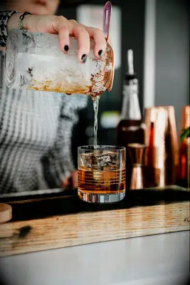 Bartender pouring whiskey sour drink into glass 