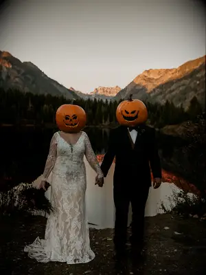 bride and groom hold hands with mountain scene in the background wearing jack o lantern pumpkins on their heads