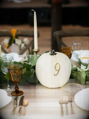 fall wedding tablescape with greenery, taper candles and white pumpkin painted with the number 9 in gold