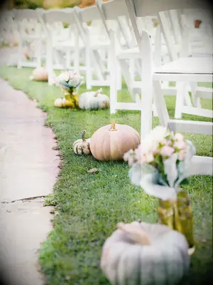 outdoor wedding ceremony aisle with pale green and orange pumpkins on the ground at the end of each chair row