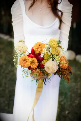 fall wedding bouquet with orange mums, chamomile flowers and long yellow ribbons