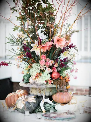 tall wedding centerpiece with seasonal orange and green fall flowers in low stone vase surrounded by pumpkins, candles and deer antlers