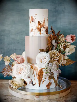 rustic fall wedding cake with painted cowhide-inspired design and pastel blush roses with dried grass