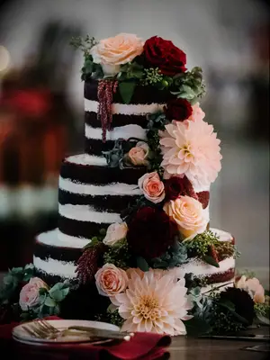 chocolate naked wedding cake decorated with pink dahlias, red roses and burgundy amaranthus