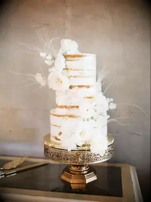 simple rustic fall wedding cake with naked buttercream frosting, white ostrich feathers and white flowers