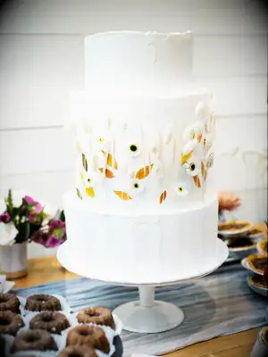 three-tier white buttercream fall wedding cake decorated with dried orange and yellow leaves and bleached bunny tail grass