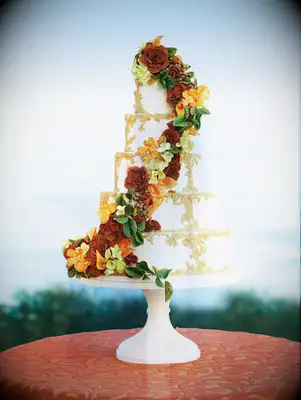 luxury fall wedding cake with gold embellishments and red and orange sugar flowers