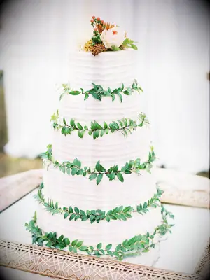 five-tier white buttercream wedding cake with greenery in between each tier and light pink rose on top