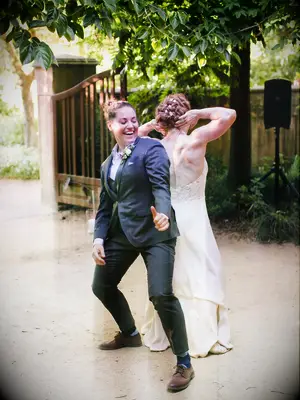 Same sex couple enthusiastically dancing to first dance song at wedding reception