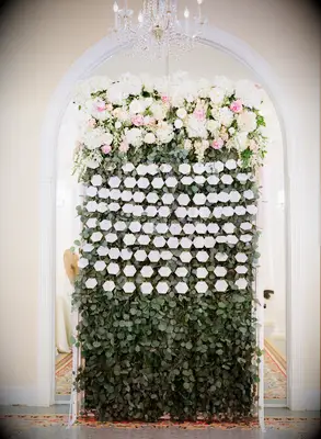 Lush eucalyptus and rose flower wall at a reception.