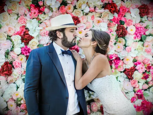 Bride and groom kiss in front of wedding flower wall photo booth.