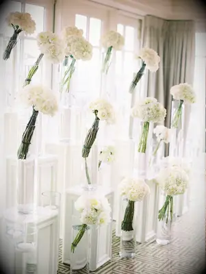 White flowers in clear vases on pillars as a flower wall idea. 