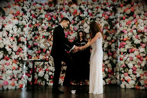 Bride and groom getting married in front of a colorful wedding flower wall.
