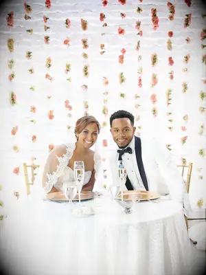 Bride and groom smiling in front of carnation flower wall.