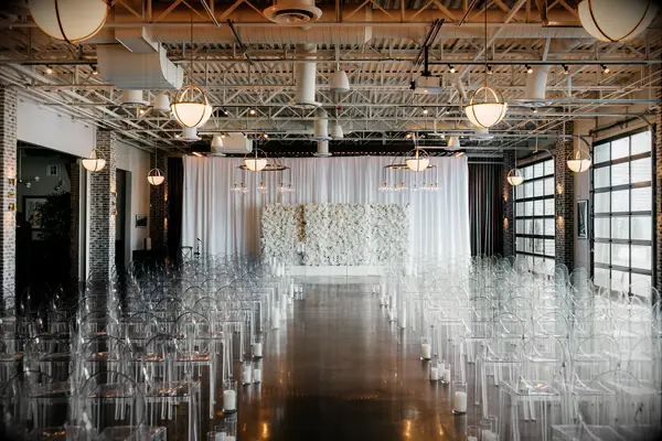 Wedding ceremony in loft with acrylic ghost chairs and white flower wall backdrop
