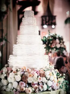 White ruffled cake on a cake stand with white, pink and blush roses