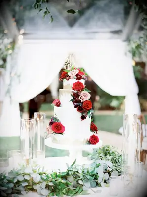 Three-tier white and gold wedding cake with a cascade of red roses