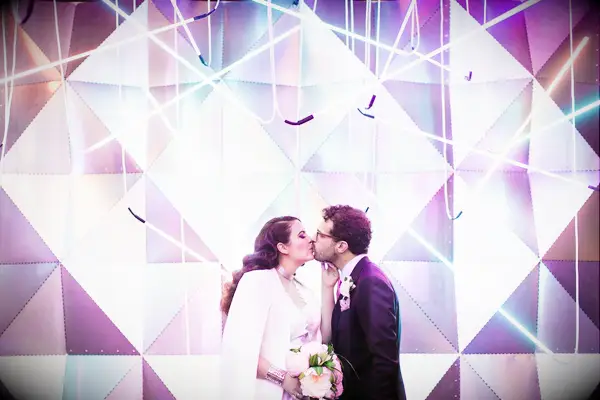 Couple kiss in front of an abstract photo booth backdrop. 