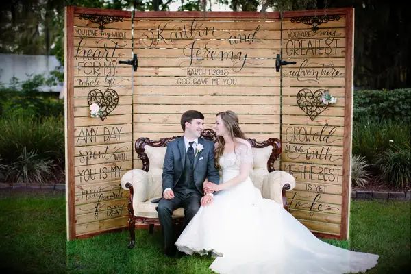 Couple poses in front of custom wooden photo booth backdrop. 